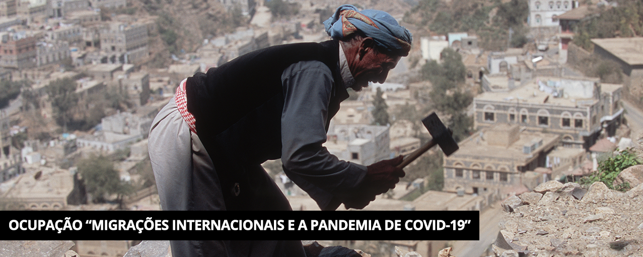 Com construções abaixo e ao fundo, um homem árabe, com vestes da região, segura um martelo. Tarja preta com Ocupação "Migrações Internacionais e a pandemia de COVID-19" escrito em branco